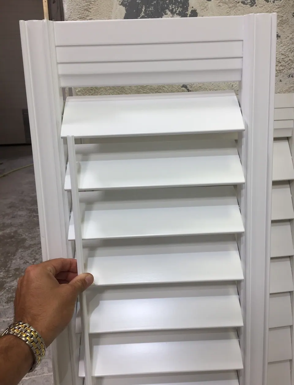A white shutter panel with a moulded frame and 4½-inch louvers tilted open, held by a tilt rod set near the left stile.